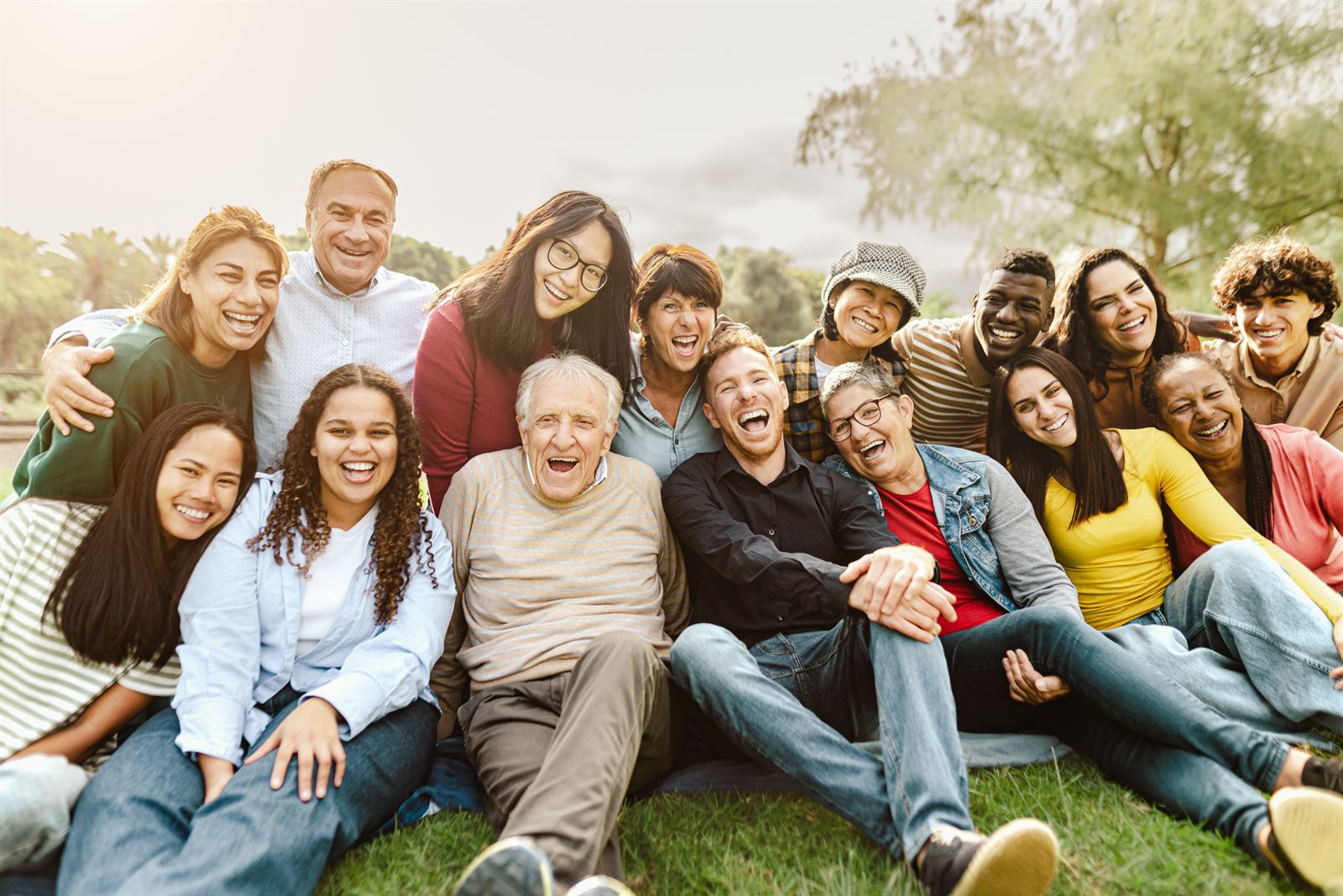 Large group of friends of all ages sitting together on the grass, laughing